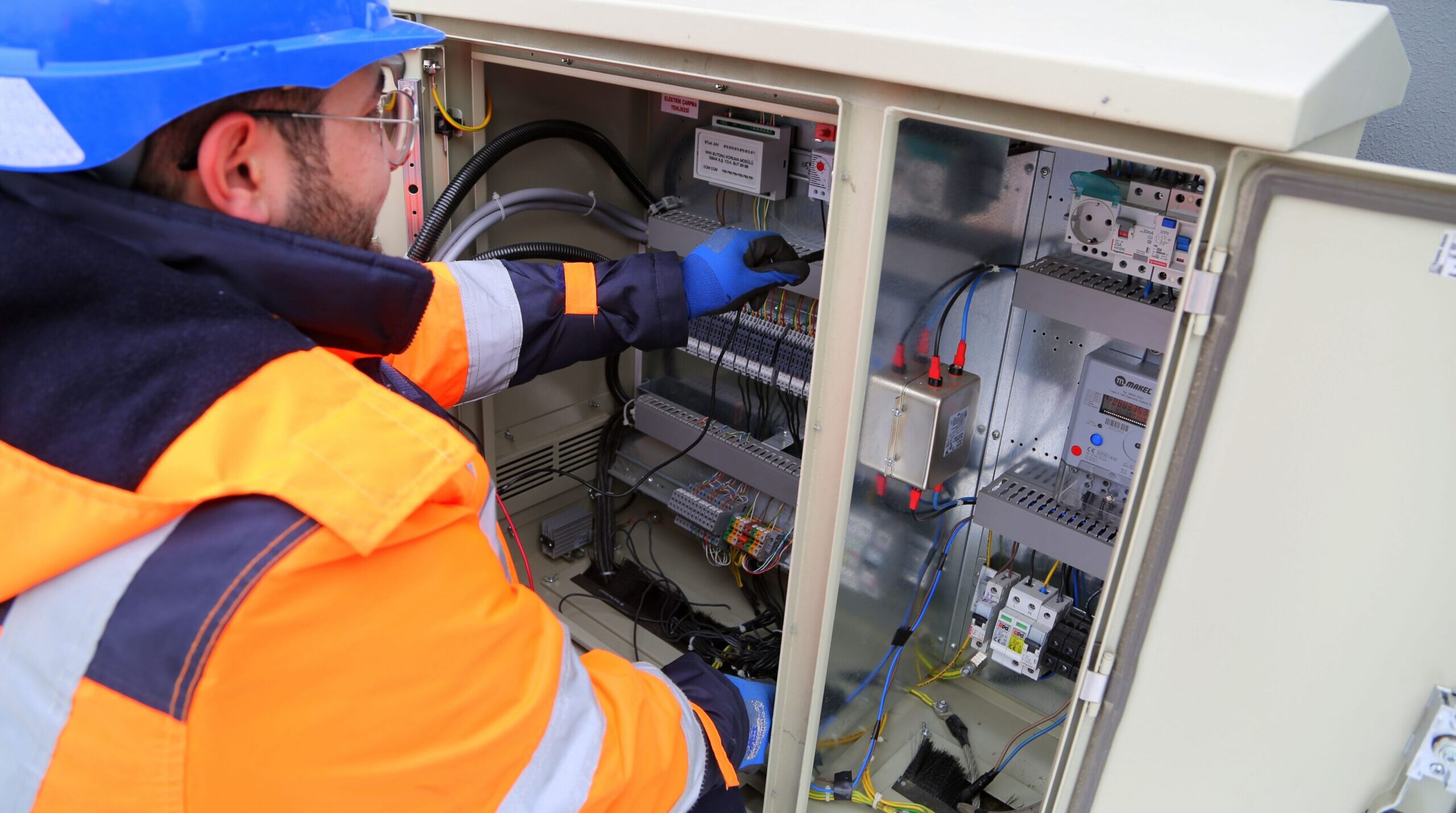 Engineer in safety gear working on an outdoor electrical panel, ensuring system functionality.